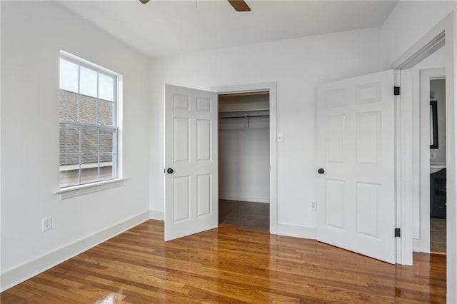 unfurnished bedroom with a closet, a spacious closet, a ceiling fan, wood finished floors, and baseboards