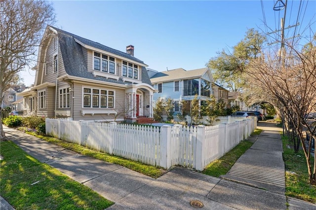 view of front of property featuring a fenced front yard, roof with shingles, a chimney, and a gambrel roof