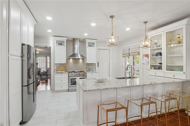 kitchen with appliances with stainless steel finishes, white cabinetry, a sink, wall chimney range hood, and a peninsula