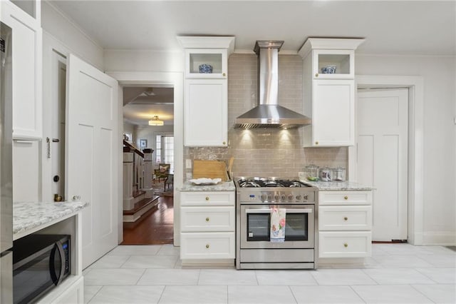 kitchen featuring wall chimney range hood, light stone countertops, stainless steel gas range oven, and tasteful backsplash