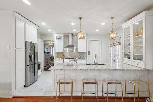 kitchen featuring a peninsula, wall chimney range hood, gas range oven, stainless steel fridge, and glass insert cabinets