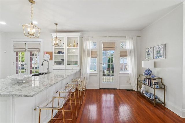 kitchen with glass insert cabinets, dark wood-type flooring, white cabinetry, a sink, and light stone countertops