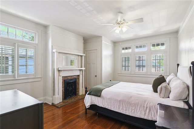 bedroom with multiple windows, a ceiling fan, a fireplace, and wood finished floors