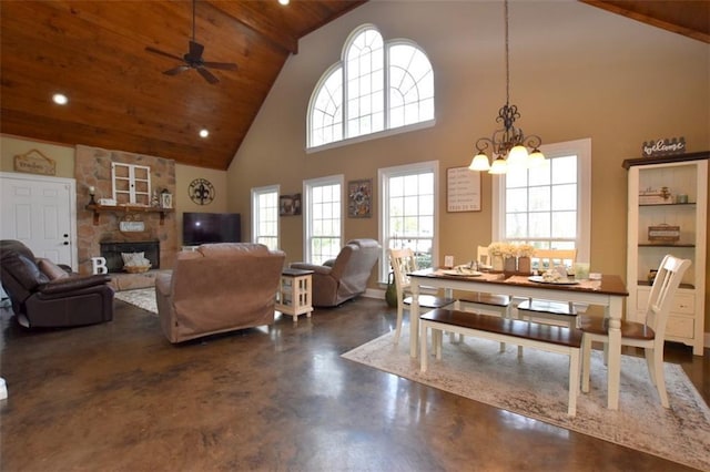 interior space featuring wood ceiling, finished concrete floors, a stone fireplace, high vaulted ceiling, and ceiling fan with notable chandelier