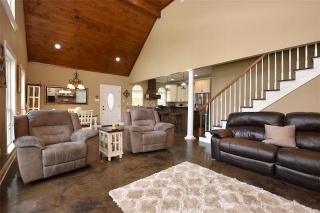 living room featuring high vaulted ceiling, stairs, concrete flooring, ornate columns, and a chandelier