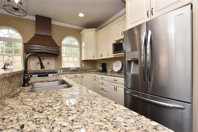 kitchen with premium range hood, a sink, appliances with stainless steel finishes, light stone countertops, and crown molding