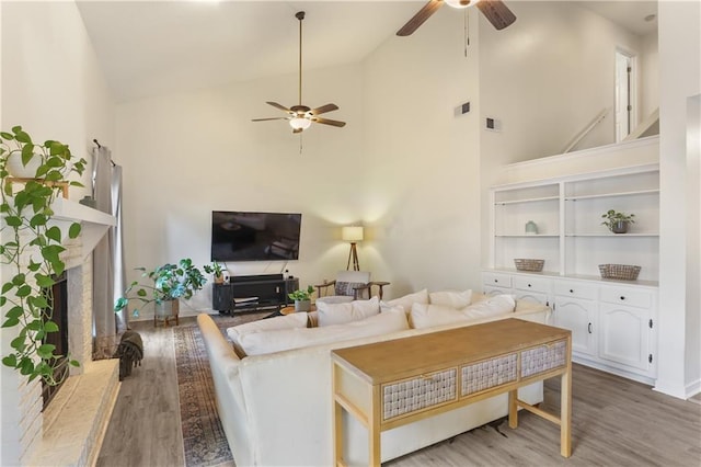 living room with ceiling fan, high vaulted ceiling, a brick fireplace, and wood finished floors