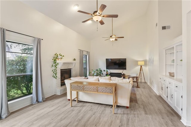 living area featuring high vaulted ceiling, a fireplace, visible vents, and light wood-style floors