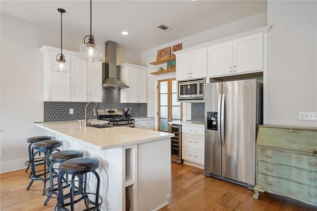 kitchen with backsplash, appliances with stainless steel finishes, a sink, wall chimney range hood, and a peninsula