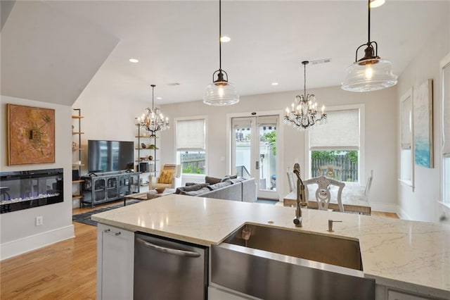 kitchen featuring stainless steel dishwasher, a sink, light stone countertops, and a notable chandelier