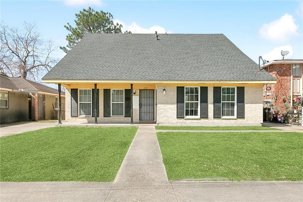 view of front of house with a shingled roof, a front lawn, and brick siding