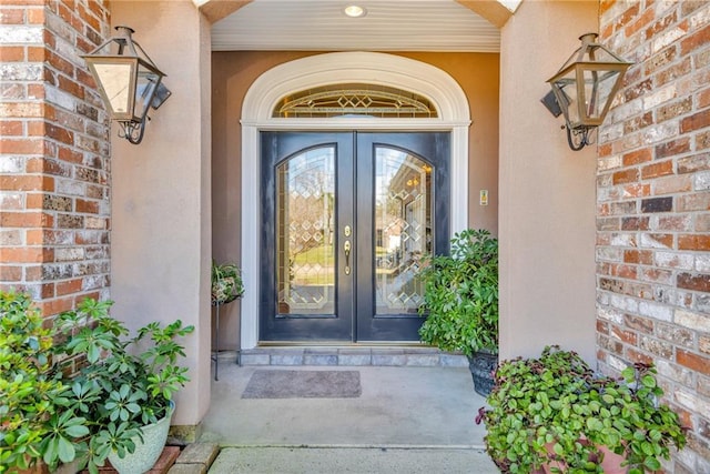 view of exterior entry with french doors, brick siding, and stucco siding