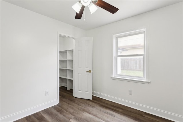 unfurnished bedroom with dark wood-style flooring, a ceiling fan, baseboards, a spacious closet, and a closet