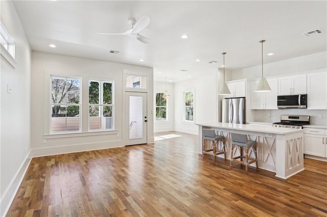 kitchen featuring visible vents, white cabinets, appliances with stainless steel finishes, a breakfast bar, and wood finished floors