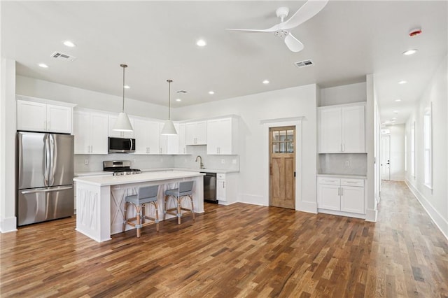 kitchen featuring appliances with stainless steel finishes, a center island, visible vents, and dark wood-type flooring