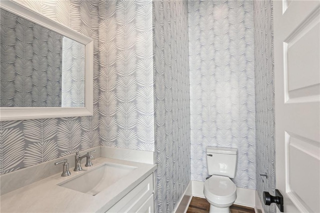 half bathroom featuring toilet, wallpapered walls, and vanity