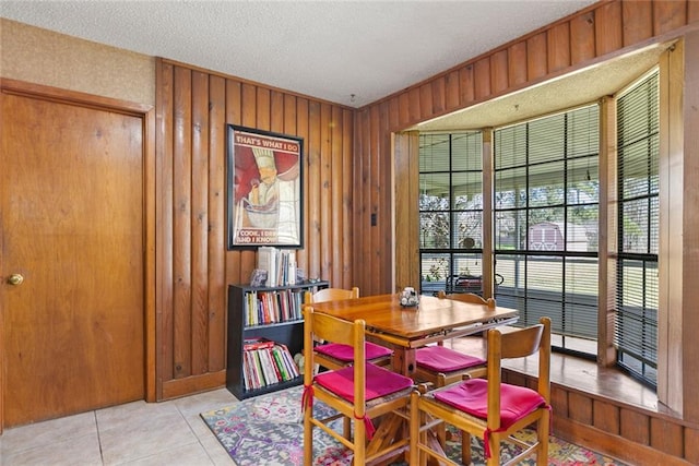 dining area with light tile patterned floors, a textured ceiling, and wood walls