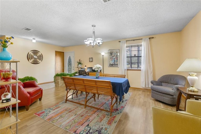 dining space with light wood finished floors, visible vents, baseboards, a textured ceiling, and a chandelier