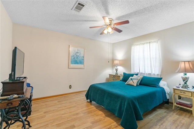 bedroom featuring baseboards, visible vents, a textured ceiling, and light wood finished floors