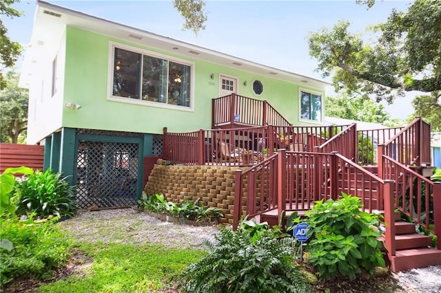 view of front facade with stairs, fence, a wooden deck, and stucco siding