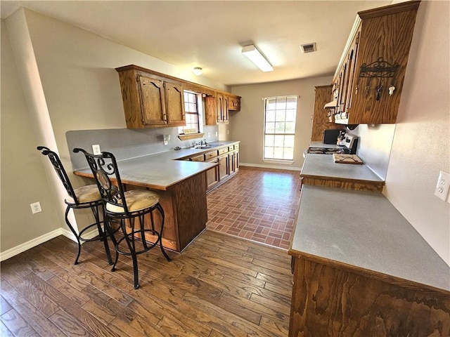 kitchen featuring visible vents, dark wood-type flooring, range with electric cooktop, a peninsula, and baseboards