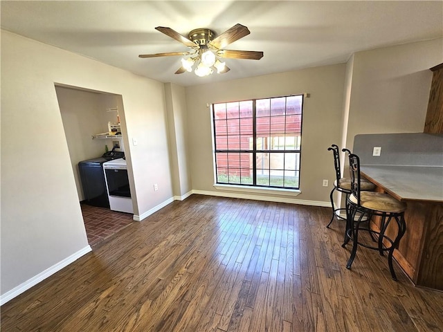 dining space with dark wood-type flooring, washer and dryer, baseboards, and a ceiling fan