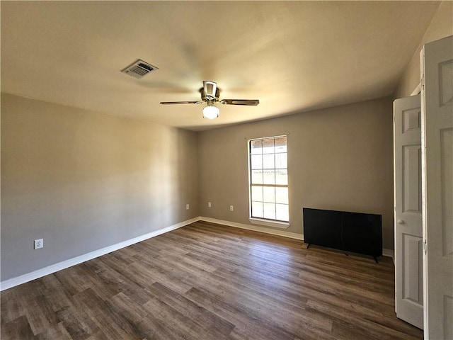 unfurnished room featuring dark wood-style floors, baseboards, visible vents, and ceiling fan