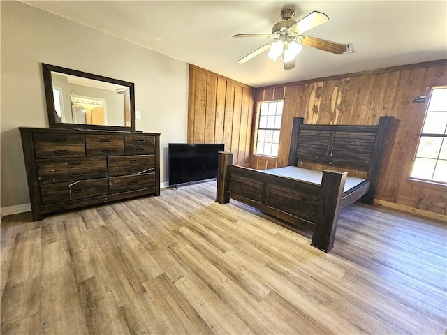 bedroom featuring a ceiling fan, wood walls, light wood-style flooring, and baseboards