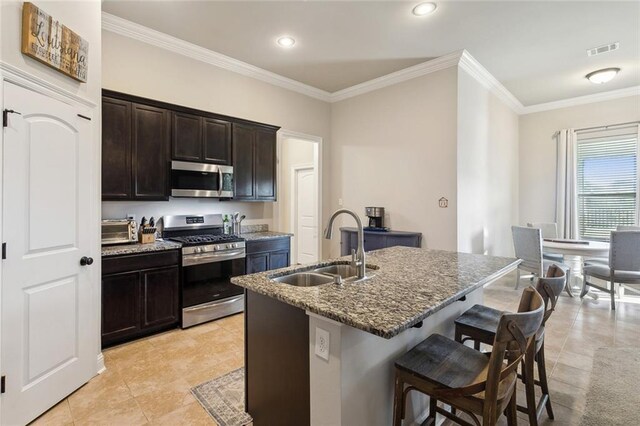 kitchen with visible vents, appliances with stainless steel finishes, a sink, dark stone countertops, and a kitchen breakfast bar