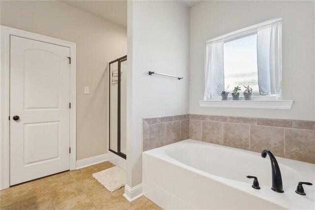 bathroom with a stall shower, baseboards, a bath, and tile patterned floors