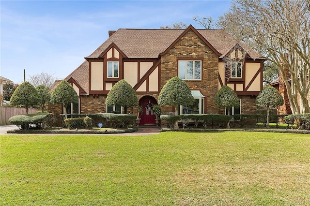 tudor-style house with a front yard, brick siding, roof with shingles, and stucco siding