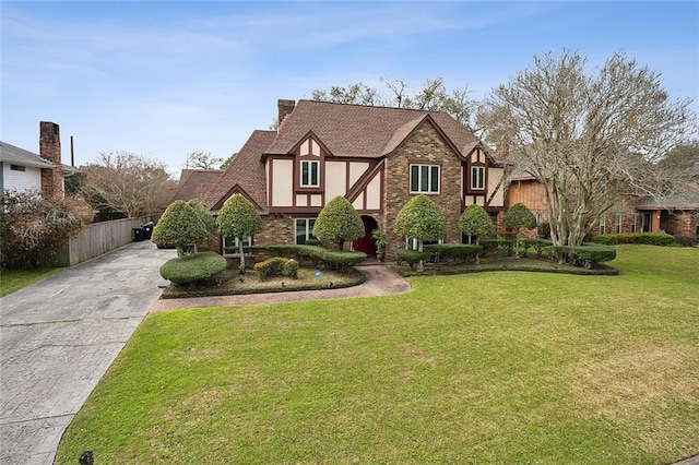 english style home with stucco siding, a front lawn, roof with shingles, concrete driveway, and brick siding