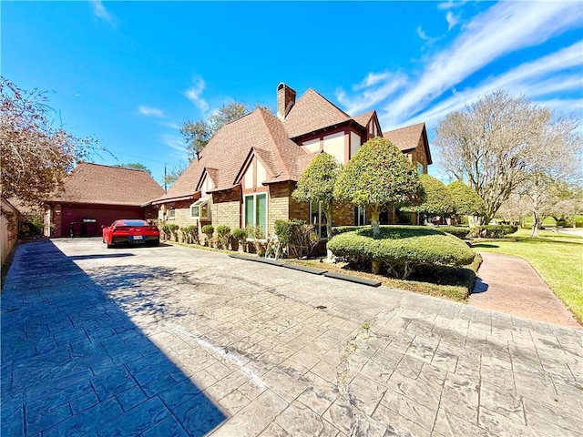 view of front of house featuring brick siding, roof with shingles, a chimney, an outbuilding, and driveway