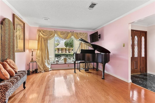 living area featuring visible vents, a textured ceiling, wood finished floors, and ornamental molding