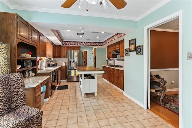 kitchen featuring gas stovetop, crown molding, under cabinet range hood, a raised ceiling, and stainless steel fridge