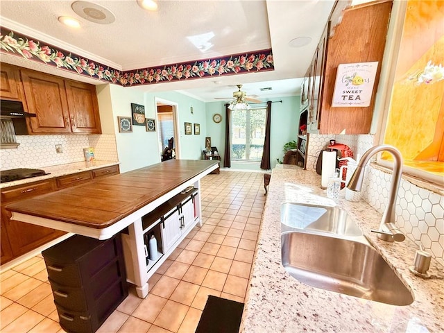 kitchen featuring under cabinet range hood, light tile patterned floors, ornamental molding, and a sink