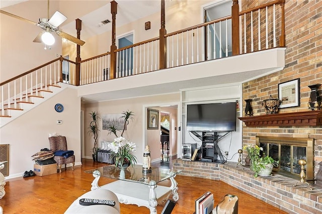 living room featuring wood finished floors, baseboards, a ceiling fan, a high ceiling, and a fireplace