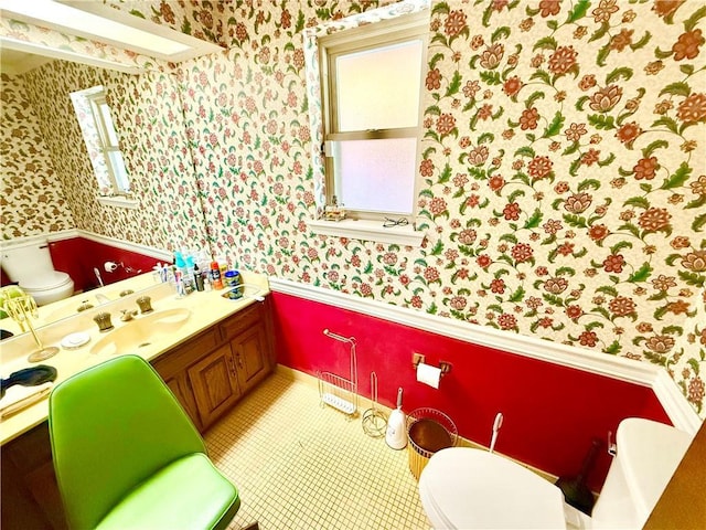 half bathroom with tile patterned floors, toilet, vanity, and wallpapered walls