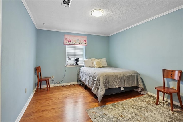 bedroom with visible vents, a textured ceiling, wood finished floors, crown molding, and baseboards