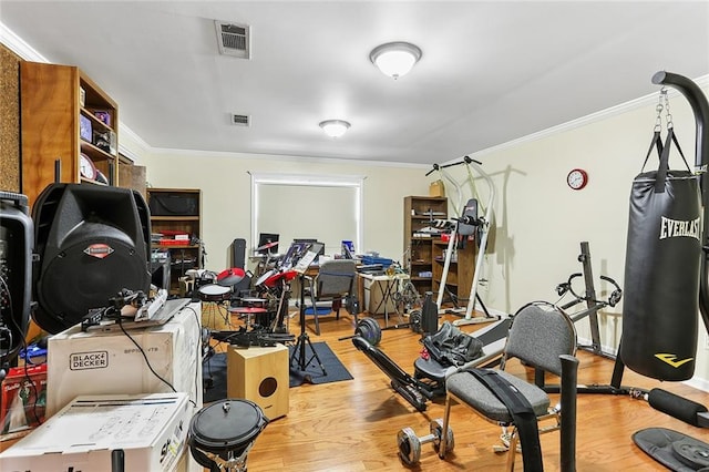 workout area with visible vents, light wood-style floors, and ornamental molding