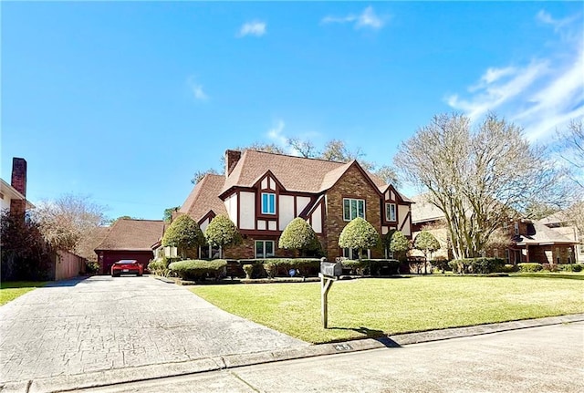 tudor-style house featuring a chimney, a front lawn, a garage, aphalt driveway, and brick siding