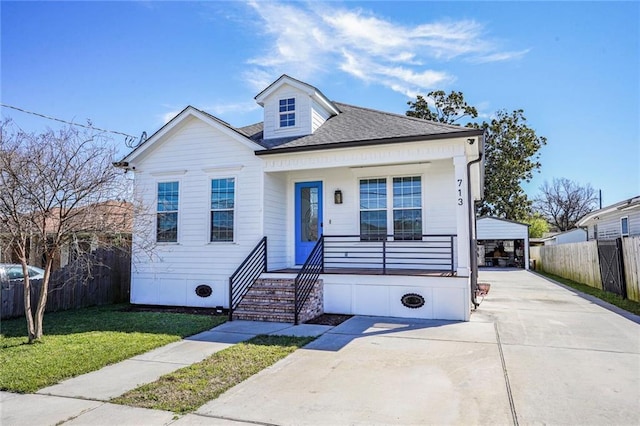 bungalow-style home featuring roof with shingles, a detached garage, covered porch, fence, and a front lawn