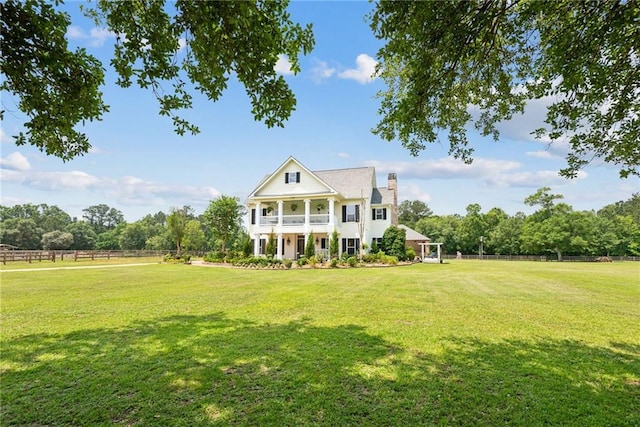 view of front of house with a chimney, a front yard, fence, and a balcony