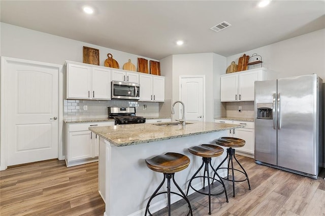 kitchen with stainless steel appliances, a sink, visible vents, light wood-style floors, and a kitchen bar