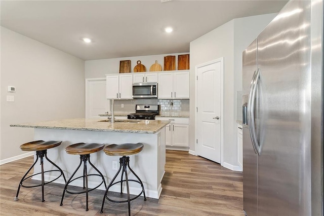 kitchen with a breakfast bar, stainless steel appliances, decorative backsplash, and wood finished floors