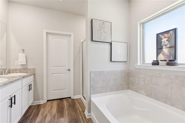 bathroom with a garden tub, wood finished floors, a sink, baseboards, and double vanity