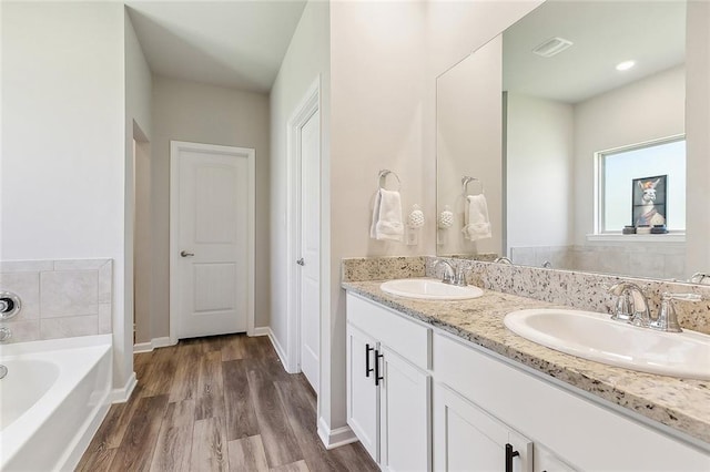 bathroom featuring a garden tub, visible vents, a sink, and wood finished floors