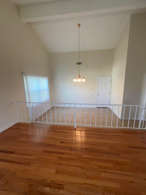 unfurnished room with an inviting chandelier, beam ceiling, high vaulted ceiling, and wood finished floors