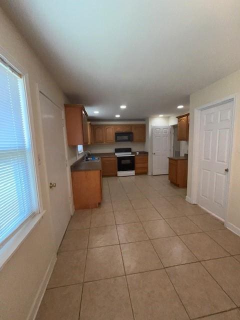 kitchen featuring light tile patterned floors, electric range oven, brown cabinetry, a sink, and black microwave