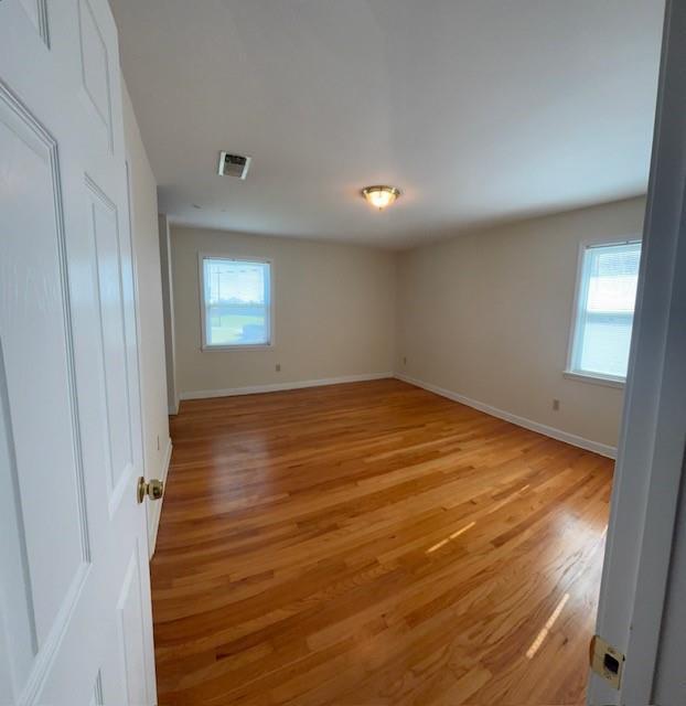 unfurnished room featuring light wood finished floors, plenty of natural light, visible vents, and baseboards